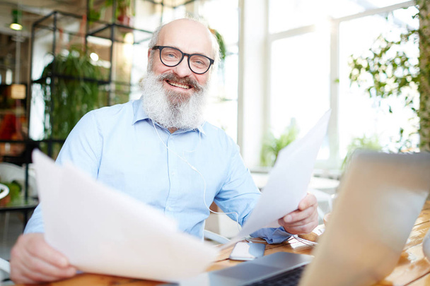 Cheerful mature man with business papers looking at camera with smile while working in cafe - Foto, Imagem