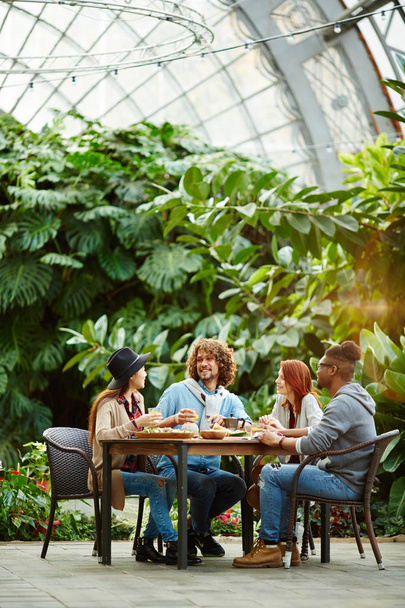 Grupo de jóvenes amigables reunidos por la mesa en el jardín para almorzar juntos en casa
 - Foto, imagen