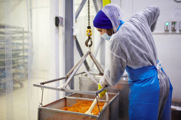 Equipe da fábrica de peixe em macacões misturando caviar vermelho em grande recipiente no departamento de produção
 - Foto, Imagem