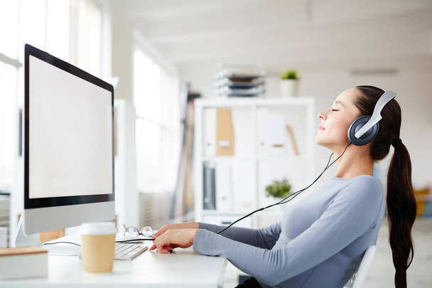 Feliz joven trabajadora de oficina disfrutando escuchando su música relajante favorita en los auriculares en el descanso
 - Foto, Imagen