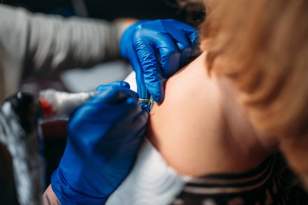 tatuador femenino en guantes estériles azules haciendo tatuaje por máquina, maestro en salón, proceso de tatuaje profesional en estudio
 - Foto, imagen