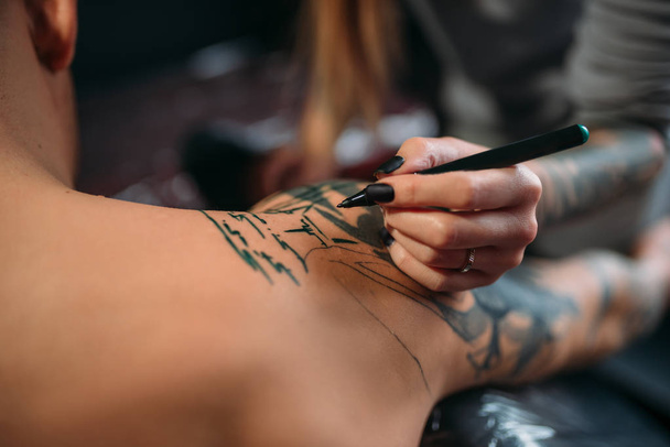 Tatuaggio femminile che fa tatuaggi a macchina sulla spalla maschile. Tatuaggio professionale nel salone
 - Foto, immagini