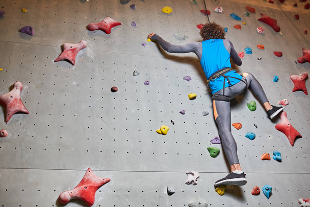 Wand für Sportklettern und aktive Person, die sich während des Trainings nach oben bewegt - Foto, Bild