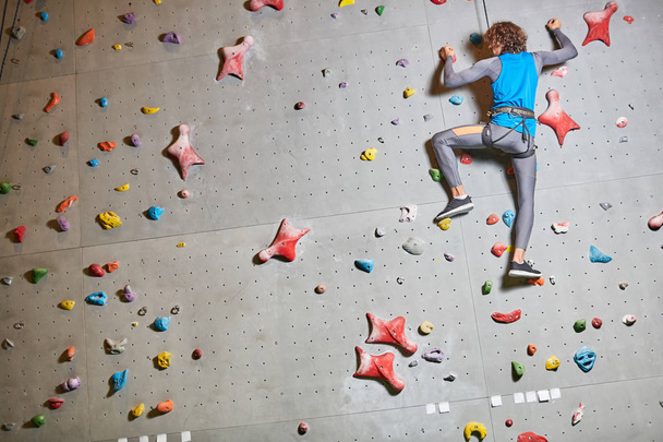 Zadní pohled na mladý dobrodruh v oblasti sportovní oblečení, které drží ruce při lezení na stěně - Fotografie, Obrázek