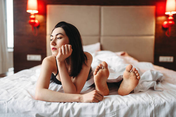 γυναίκα εσώρουχα ξαπλωμένη στο κρεβάτι εναντίον αρσενικό πόδια, οικειότητα στο υπνοδωμάτιο - Φωτογραφία, εικόνα