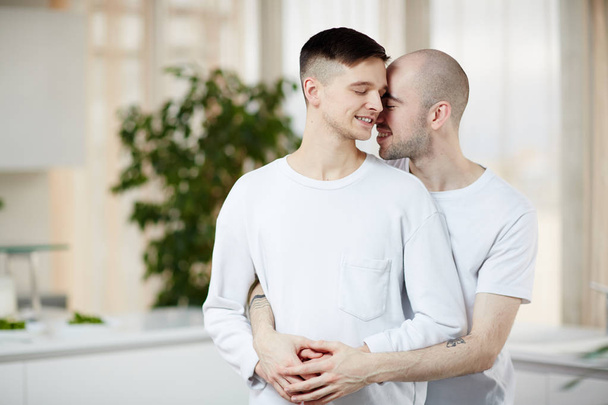 Ερωτική γκέι άνδρες στέκεται στην αγκαλιά με τα μάτια τους κλειστά και χαμογελαστός - Φωτογραφία, εικόνα