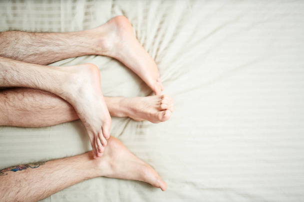 Πόδια και τριχωτά πόδια ομοφυλόφιλο ζευγάρι κατά τη διάρκεια του ύπνου στο κρεβάτι - Φωτογραφία, εικόνα