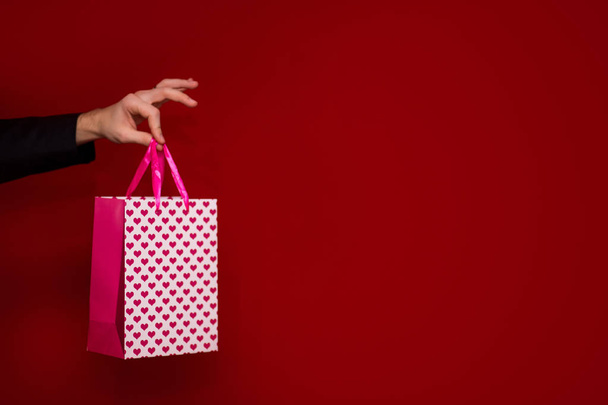 Mężczyzny ręką przytrzymaj miłości prezent torba, z czerwonym tle, skupić się na prezent torba. Walentynki-dzień składu - Zdjęcie, obraz