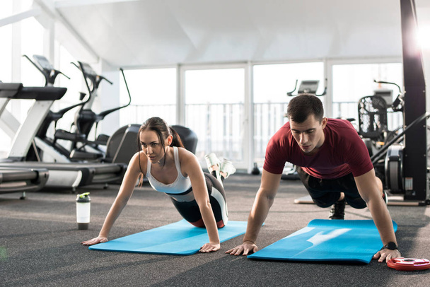 Portrait of young sports couple pushing up on mats in modern gym - Photo, Image