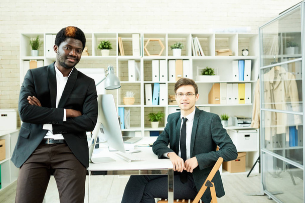 Multi-ethnic team of white collar workers wearing stylish suits posing for photography while gathered together in modern open plan office - Fotografie, Obrázek
