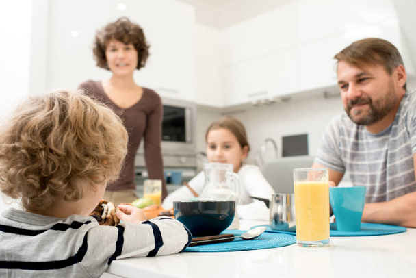 2 人の子供は、自宅で朝食を楽しんで幸せな若い家族の肖像居心地の良いキッチンで夕食のテーブルに座っている、金髪の少年を見て - 写真・画像