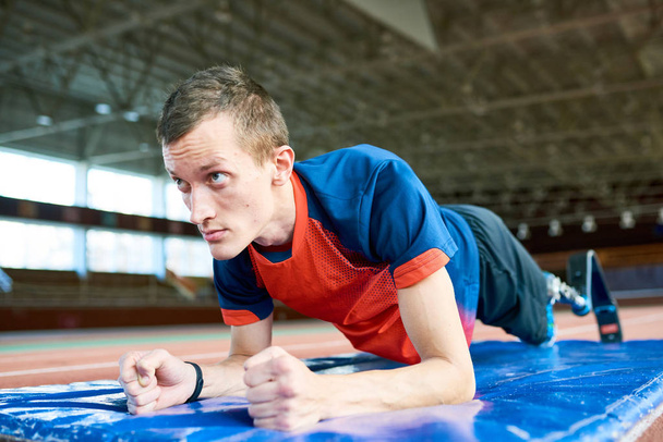 Retrato de deportista amputado determinado haciendo entrenamiento de ejercicio de tablón para Paralímpicos en estadio interior moderno
 - Foto, Imagen