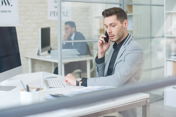 Portret widok strony młody biznesmen, praca przy biurku mówiąc przez telefon i za pomocą komputera w nowoczesne Biuro, miejsce - Zdjęcie, obraz