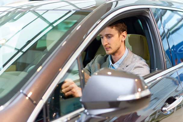 Портрет красивого молодого человека, сидящего внутри роскошного автомобиля, тестирующего его в выставочном зале перед покупкой
 - Фото, изображение