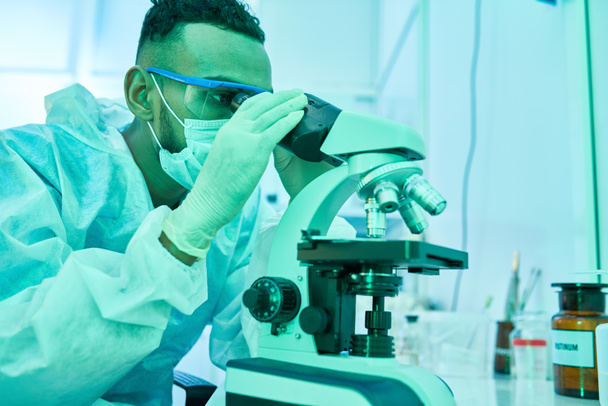 Porträt eines jungen Wissenschaftlers aus dem Nahen Osten, der während seiner Arbeit im Labor in die Mikroskopie schaut - Foto, Bild