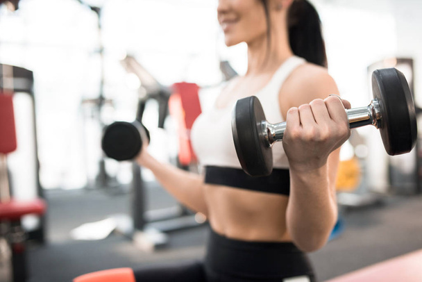 Close up of sportive young woman  training with dumbbells in modern gym, focus on heavy dumbbell in hand - Foto, Imagem