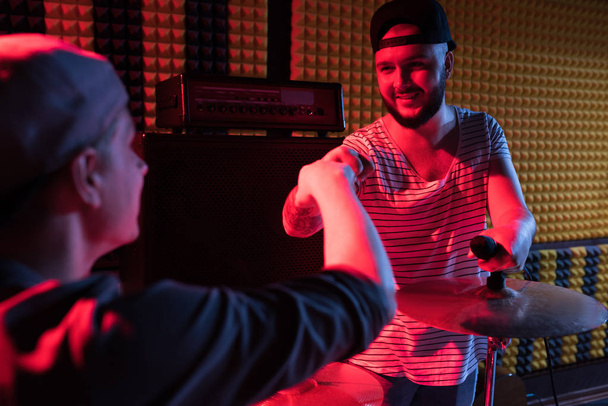 Portrait d'un chanteur moderne tatoué qui joue du tambour tout en répétant dans un studio d'enregistrement sombre
 - Photo, image