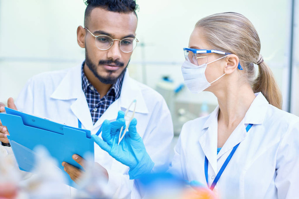 Portret van twee jonge wetenschappers, een van hen Midden-Oosten, samen te werken in medisch laboratorium onderzoek gedaan op chemische stoffen en bacteriën - Foto, afbeelding