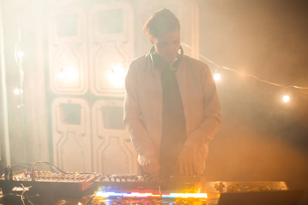 Frontansicht Porträt eines trendigen jungen DJs, der im verrauchten Nachtclub am Mischpult Musik spielt, Kopierraum - Foto, Bild