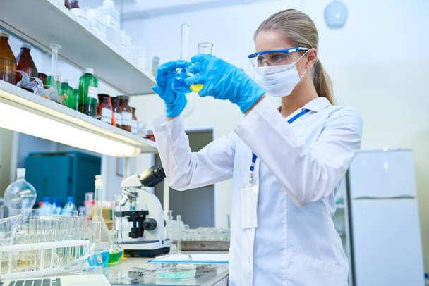 Retrato de cientista muito feminino usando máscara protetora trabalhando com tubos de ensaio estudando produtos químicos em laboratório médico, espaço de cópia
 - Foto, Imagem