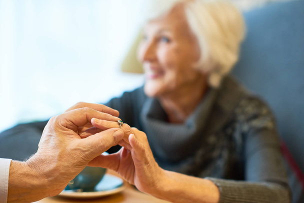 Close-up shot van ouderen verloofde vinger van mooie vrouw verlovingsring zetten tijdens de vergadering op restaurant, concentreren op de voorgrond - Foto, afbeelding