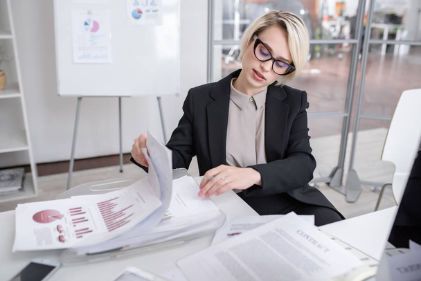 Portrait of successful blonde businesswoman discussing statistics report with colleagues looking at graphs and charts with financial data during meeting in modern office - 写真・画像
