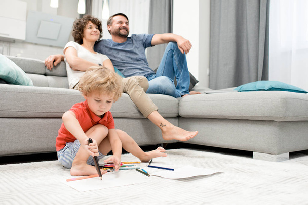 Ritratto di famiglia felice godendo serata a casa concentrarsi sul bambino disegno immagini seduto sul pavimento in soggiorno, copiare spazio
 - Foto, immagini