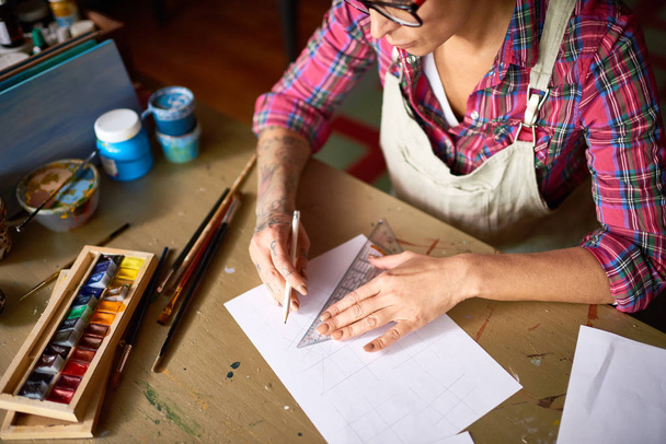 Korkea kulma tatuoitu nuori nainen laatii luonnos lyijykynällä taiteen ja veneet projekti istuu puinen pöytä työpajassa
 - Valokuva, kuva