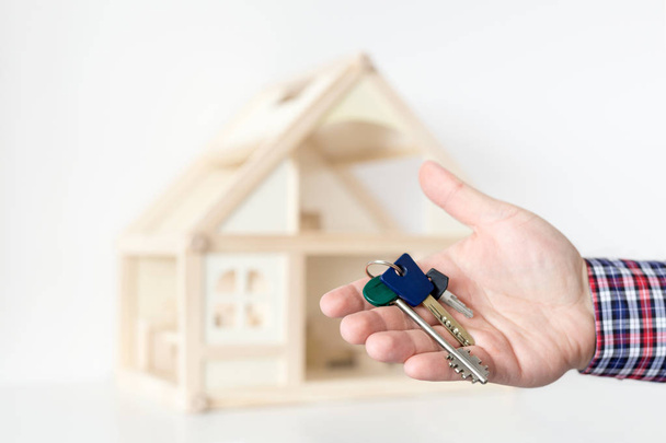Agent's hand hold keys against house model on background. - Foto, afbeelding