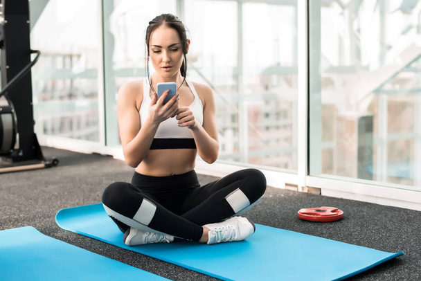 Retrato de larga duración de una joven en forma usando un smartphone durante la práctica de yoga en un gimnasio moderno
 - Foto, imagen