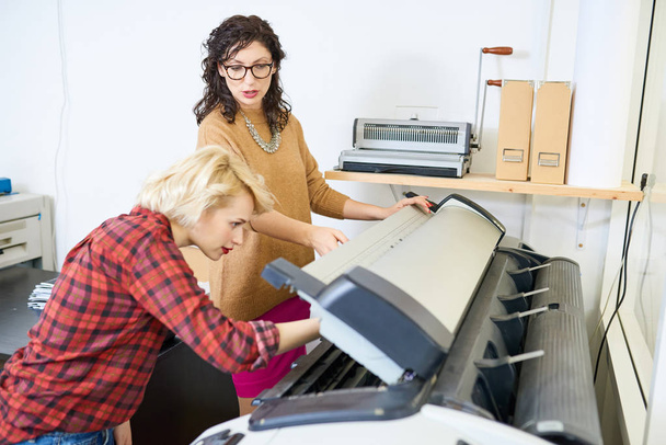 Porträt zweier Frauen, die in der Druckerei eine Plottermaschine aufstellen und sich darauf konzentrieren, dass der Manager dem Mitarbeiter Anweisungen gibt - Foto, Bild