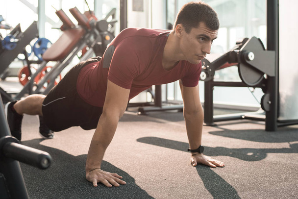 Full length portrait of handsome muscular man doing push ups training in modern gym - Photo, Image