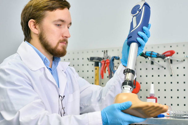 Портрет молодого протезиста, держащего протез ноги, проверяющий его на качество и корректирующий при работе в современной лаборатории
 - Фото, изображение