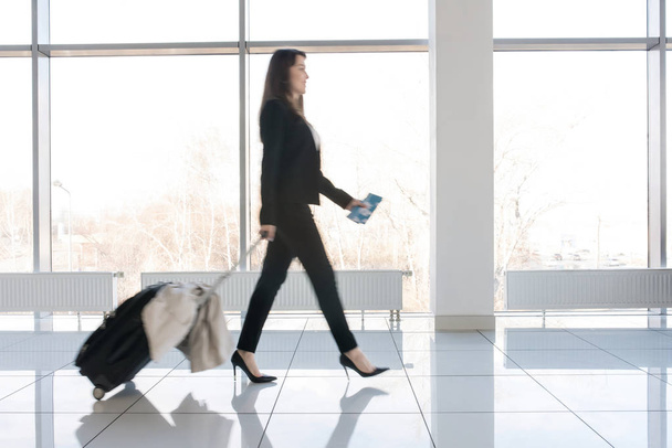 Вид сбоку: красивая бизнесвумен с чемоданом шагает по лоджии ожидания в современном аэропорту
 - Фото, изображение