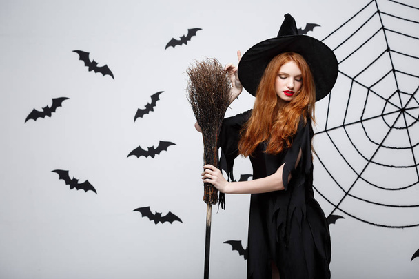 Halloween Witch Concept - Retrato de bela bruxa jovem com vassoura sobre a parede cinza com fundo de teia de morcego e aranha
. - Foto, Imagem