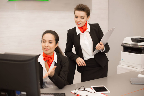 Portret van twee mooie vrouwelijke ondernemers dragen zwarte en rode uniform met behulp van computer op Bureau in moderne kantoor internet zoekt werk - Foto, afbeelding