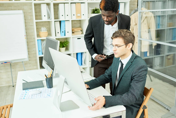 Портрет двох успішних підприємців, один з них Африканська,-американської, дивлячись на екран комп'ютера при обговоренні проекту роботи сидячи за столом у сучасні офісні - Фото, зображення
