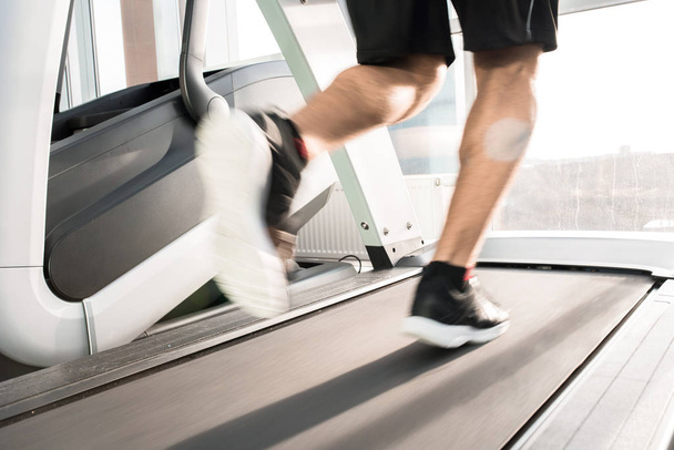 Blurred motion of muscular  male legs running on treadmill lit by sunlight - Photo, image