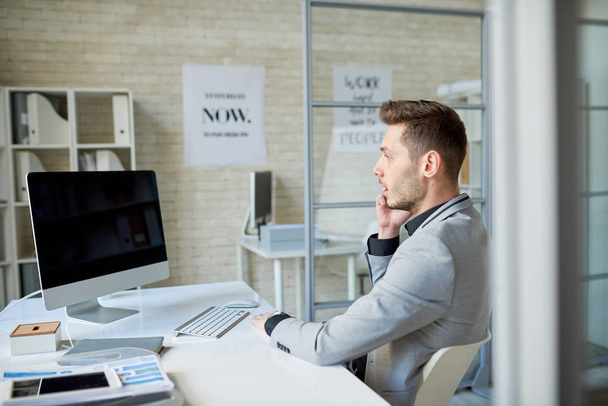 Portret widok strony udany młody biznesmen mówi przez telefon, siedząc przy biurku w nowoczesne Biuro, miejsce - Zdjęcie, obraz