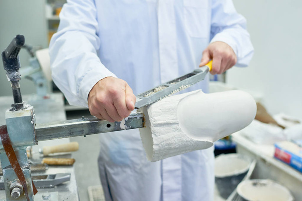 Вид спереди на середину неузнаваемого протезиста, работающего в конструкторской лаборатории по формированию формы и шлифованию части ноги
 - Фото, изображение