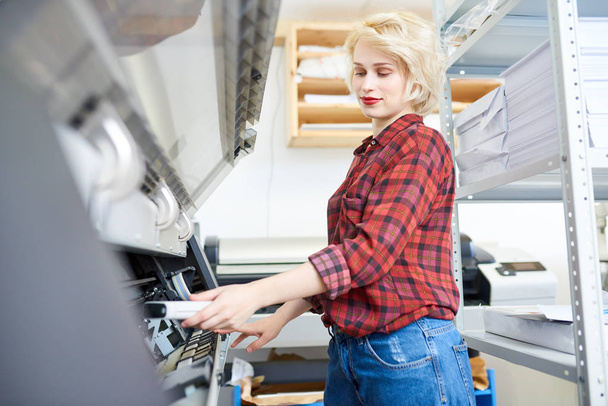 Side view portrait of modern blonde woman working with plotters in printing shop of publishing company - Φωτογραφία, εικόνα