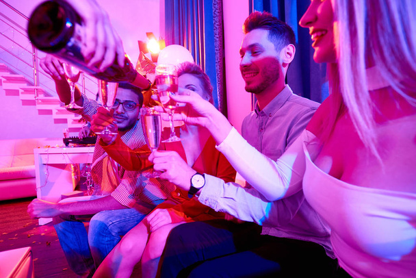 Zijaanzicht op groep glamoureuze mensen genieten van particulieren, zittend op de Bank lachen gelukkig terwijl serveerster gieten dranken - Foto, afbeelding