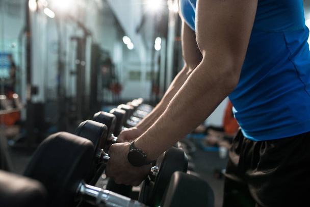Side view close up of strong male hands picking up dumbbells from equipment stand in modern gym, copy space - Foto, Bild