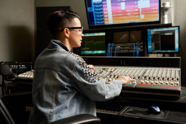 Pensivo ocupado hipster jovem mulher em jaqueta jeans trabalhando no console de mistura analógica profissional ao criar trilha sonora única em estúdio de gravação
 - Foto, Imagem