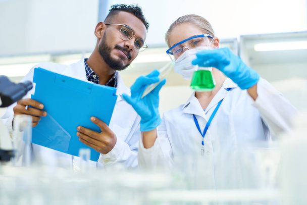 Retrato de bajo ángulo del equipo internacional de científicos trabajando juntos en laboratorio médico haciendo investigación sobre químicos y bacterias
 - Foto, Imagen