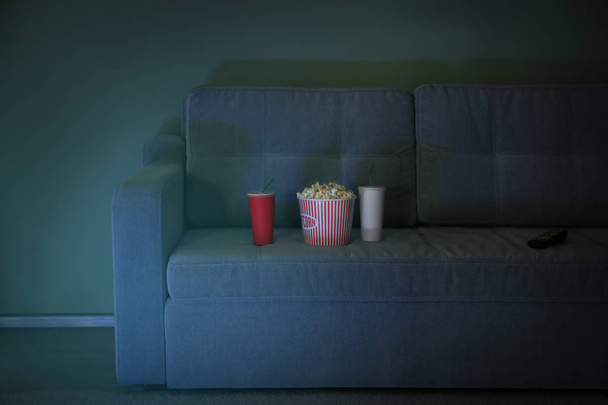 Comfortable sofa with popcorn, drinks and remote control in home cinema. Watching movie - Foto, Imagen