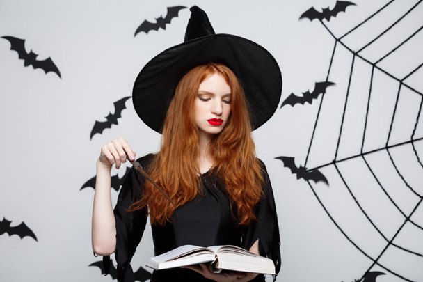 Koncepcja Halloween - piękna czarownica gry z magiczny kij na szarym tle. - Zdjęcie, obraz