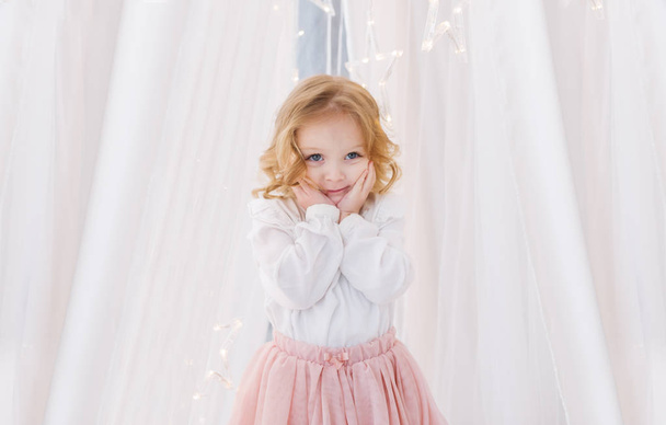 The cute little girl is  against the background of a white curtain - Photo, Image