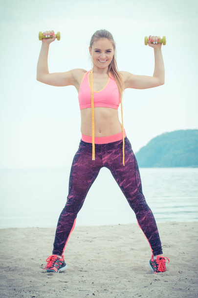 Chica delgada en ropa deportiva con centímetro haciendo ejercicio con pesas en la playa, estilo de vida deportivo
 - Foto, imagen