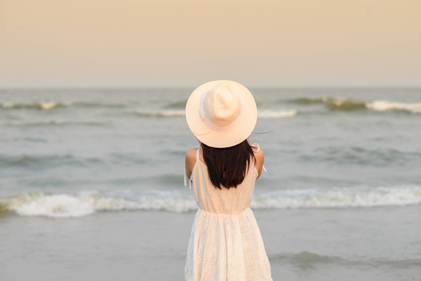 Back of woman wearing hat with white dress standing on the beach - Foto, Imagem